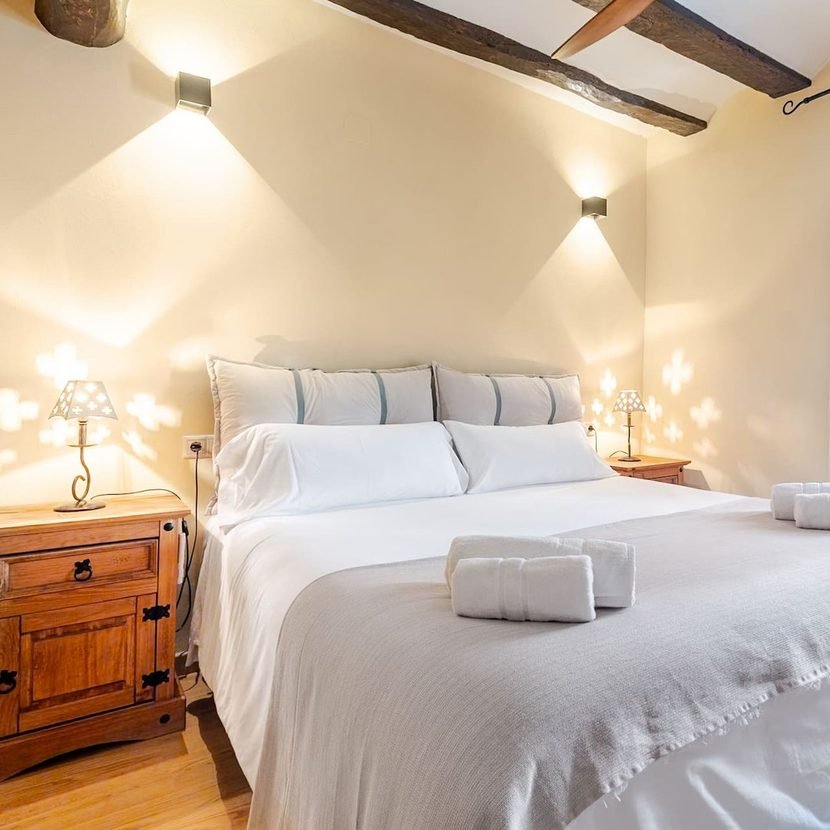 Chambre principale de l’hébergement pour professionnels à Castalla, avec lit double, table de chevet en bois et poutres apparentes