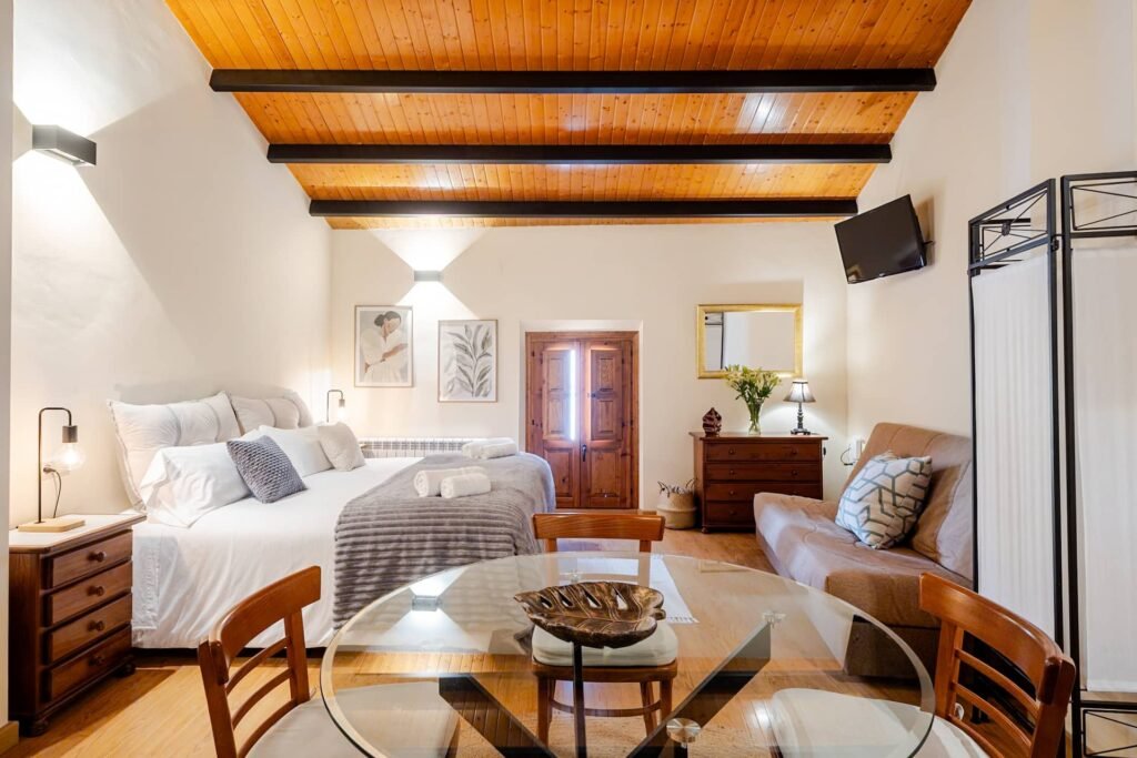 Apartamento de Casa Rural Castalla con la cama, el sofá y la mesa de cristal bajo el techo de madera