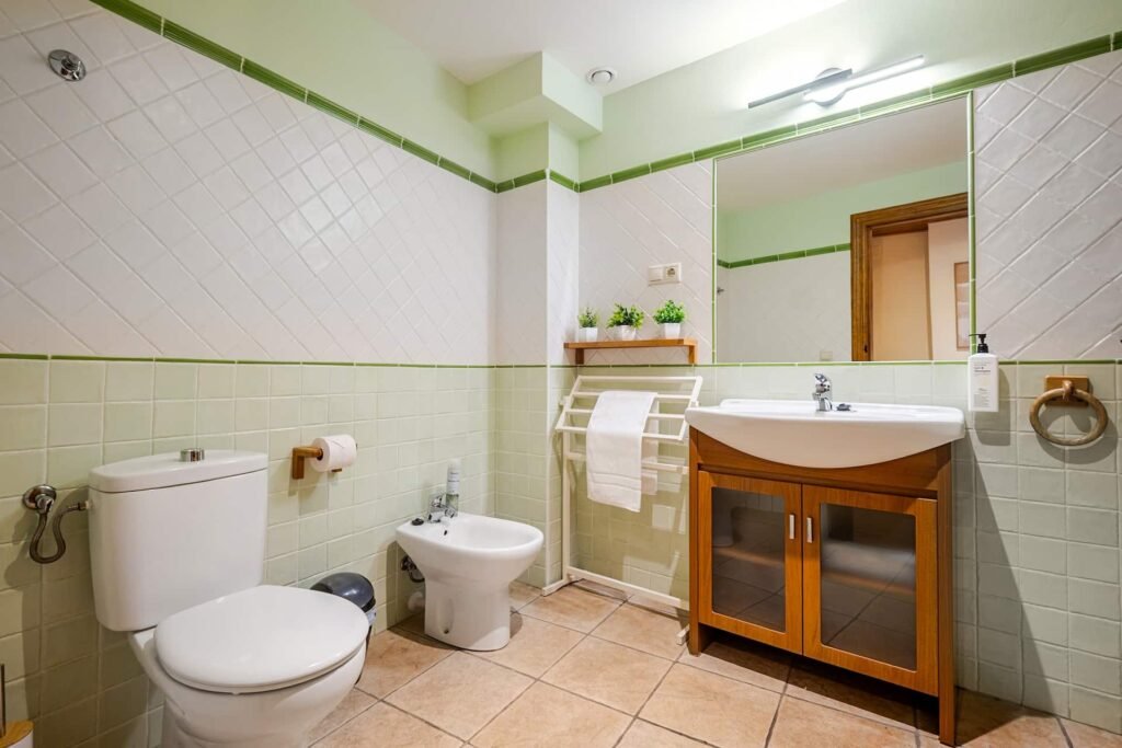 Aseo de Casa Rural Castalla con azulejo en tonos verdes, lavabo con mueble de madera y sanitarios