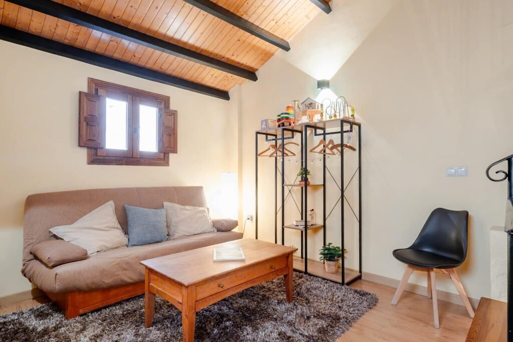 Zona de ocio y descanso de la buhardilla de Casa Rural Castalla, con sofá, mesa baja y ventana bajo el techo de madera