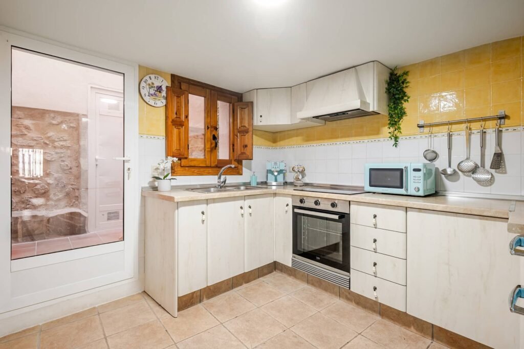 Cocina equipada de Casa Rural Castalla con azulejo amarillo, vitrocerámica, horno y puerta de acceso al patio