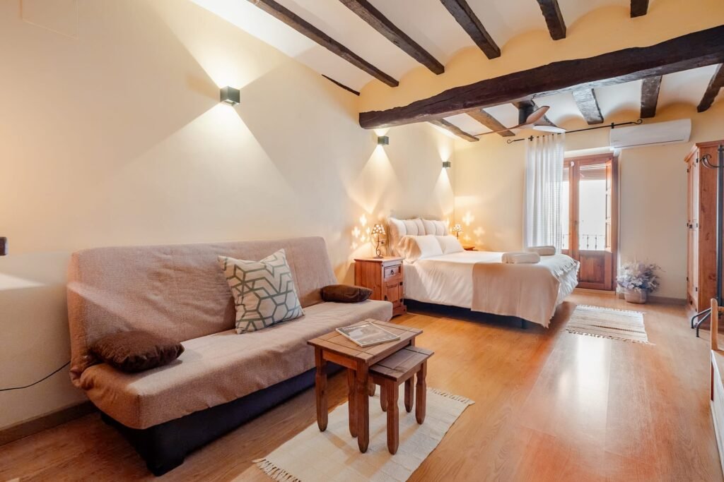 Habitación principal de Casa Rural Castalla con sofá, mesa auxiliar y la cama al fondo bajo las vigas