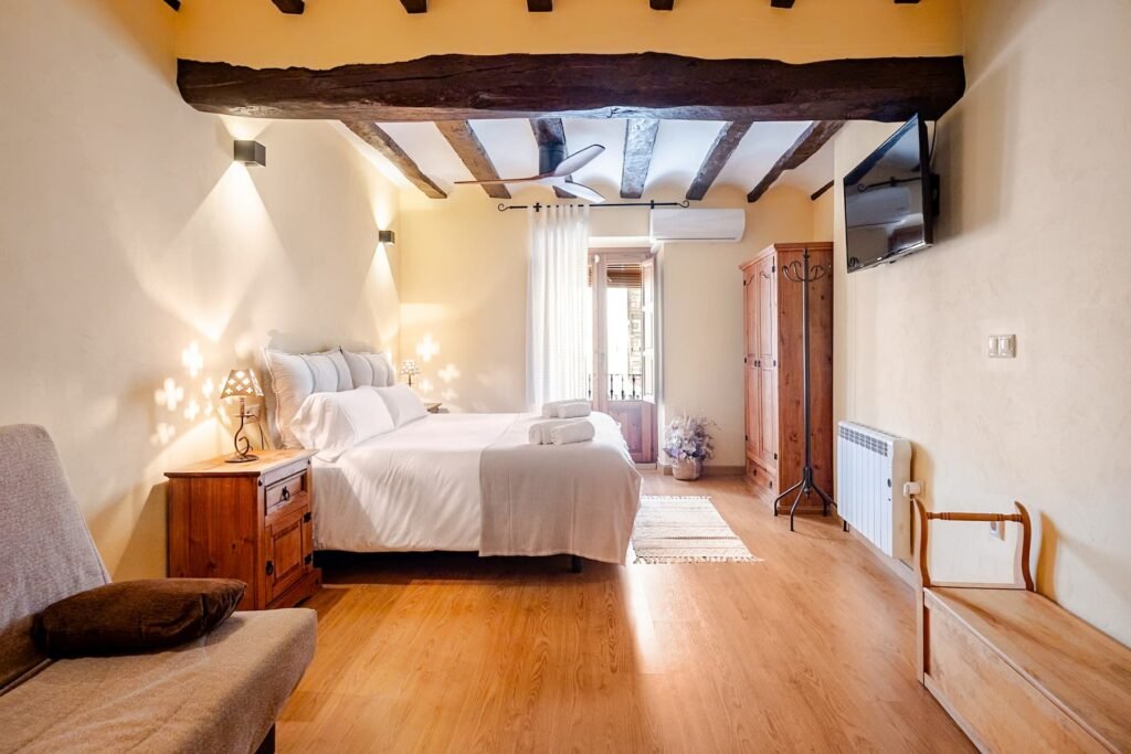 Habitación principal de Casa Rural Castalla con televisión, cama doble y balcón bajo las vigas de madera