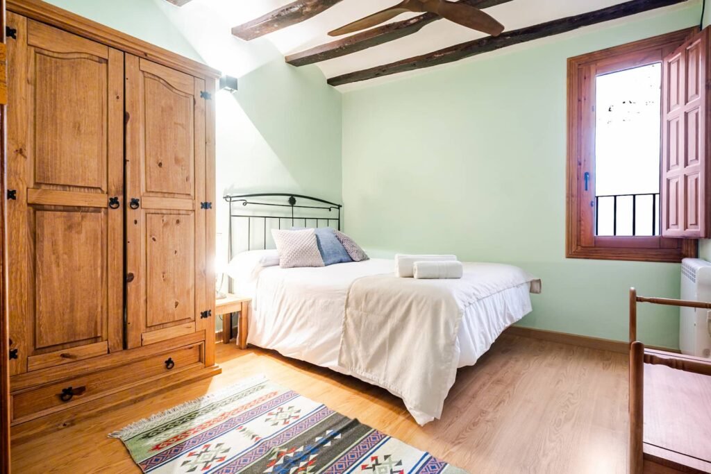 Habitación de Casa Rural Castalla en tonos verdes con vigas de madera, armario y alfombra kilim