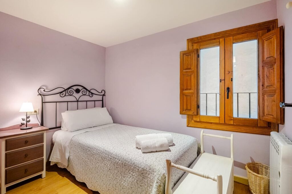 Sala de juegos de Casa Rural Castalla, en tonos malva, con cama y ventana de madera al balcón