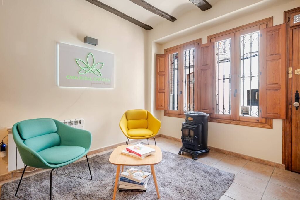 La Tardor, recepción y salón de Casa Rural Castalla, con sillones turquesa y amarillo, estufa de leña y el cartel de la casa